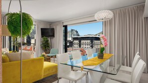 A modern living room with a glass dining table, white chairs, a yellow sofa, and a hanging plant. - Stunning Views From De Waterkant Apartment (Cape Town)