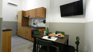 A compact kitchen with wooden cabinets, a stove, and a dining table with chairs. A flat-screen TV is mounted on the wall above the table. - Giuseppe Apartment (Rome)