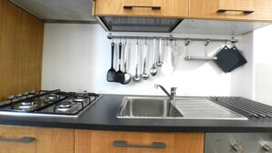 A kitchen with wooden cabinets, a gas stove, a stainless steel sink, and hanging utensils. - Giuseppe Apartment (Rome)