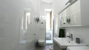 A modern bathroom with white tiles, a toilet, a sink, and a mirror. - Giuseppe Apartment (Rome)