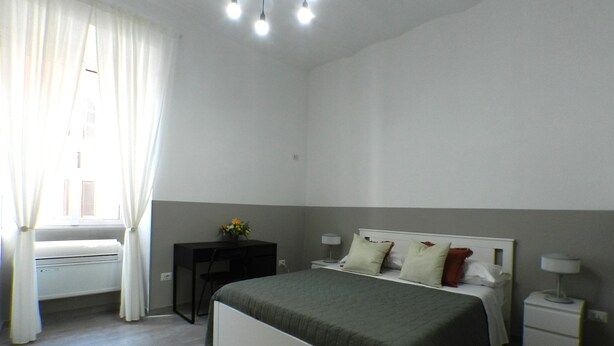 A bedroom with a bed, bedside tables, a desk, and a window with curtains. - Giuseppe Apartment (Rome)