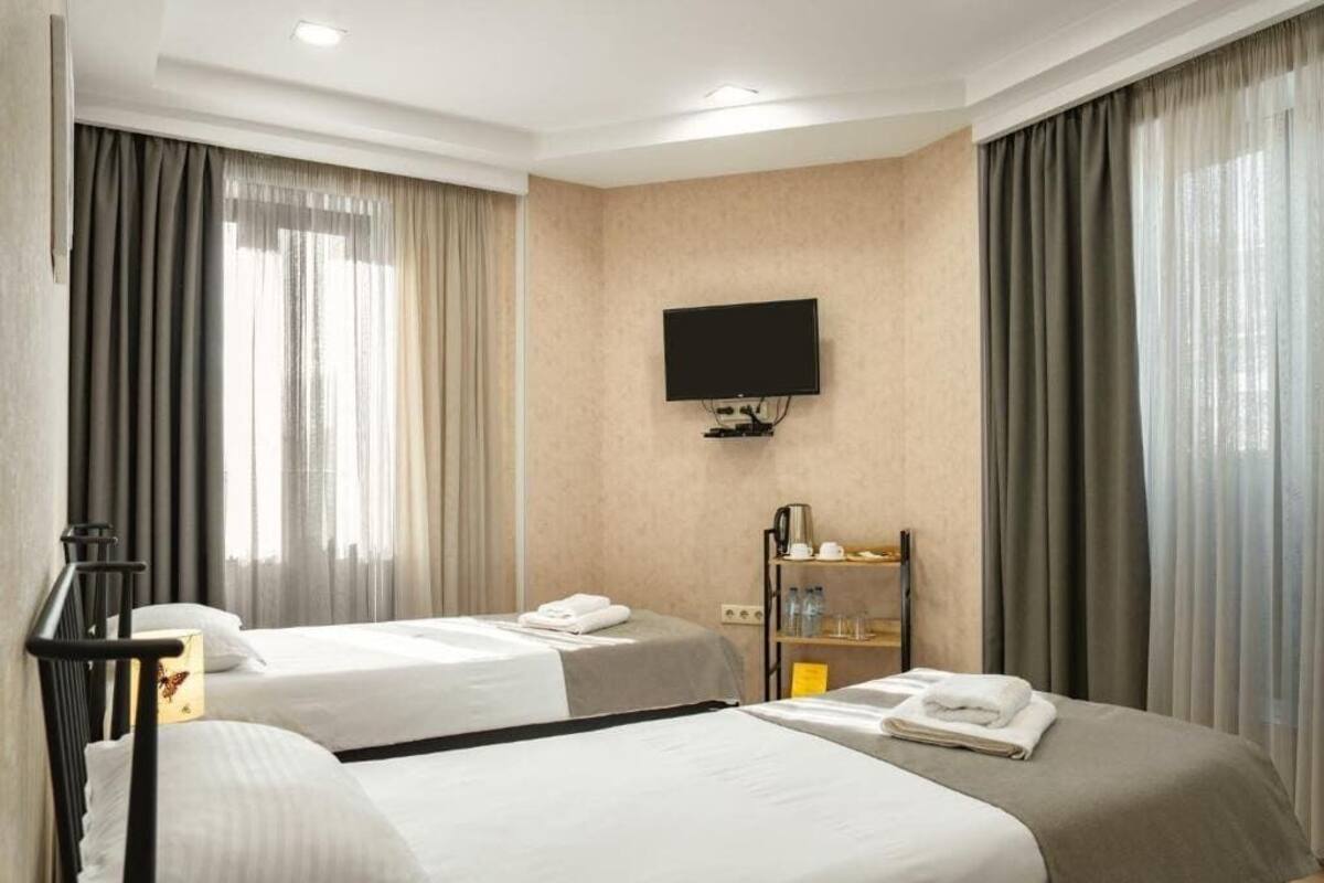 Ein Hotelzimmer mit zwei Betten, einem Fernseher, einem Schreibtisch mit Lampe und einem Regal mit Toilettenartikeln.