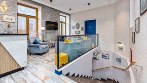 A modern interior with a kitchen area, a seating area with a sofa and armchairs, a staircase with a glass railing, and a blue door. - Monument1880 (Tbilisi)