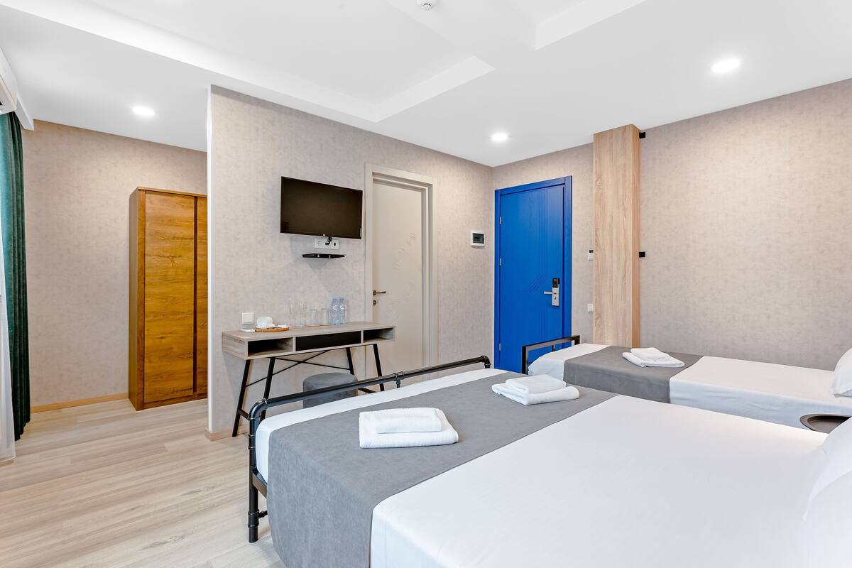Ein Hotelzimmer mit zwei Betten, einem Schreibtisch mit Flachbildfernseher, einem Holzschrank und einer blauen Tür.