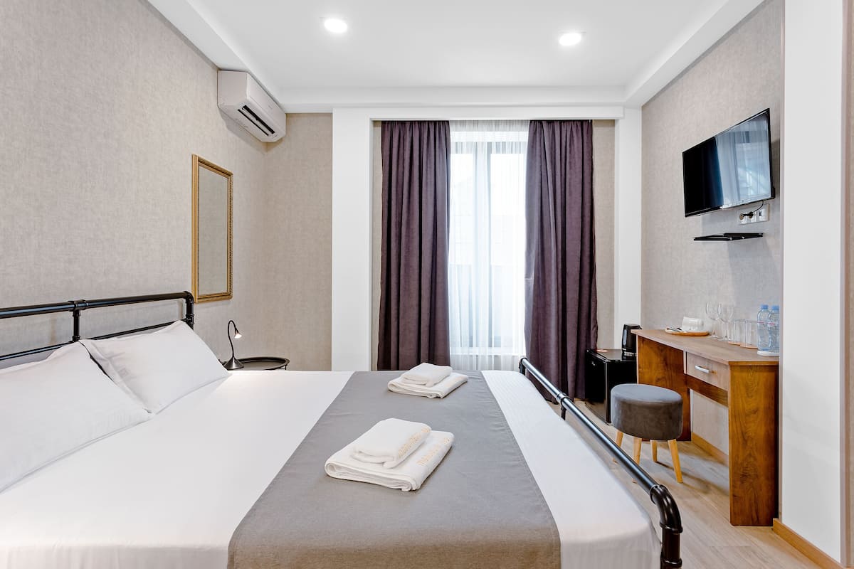 Ein Hotelzimmer mit Bett, Schreibtisch, Fernseher und einem Fenster mit Vorhängen.