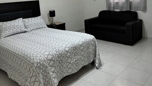 Une chambre à coucher avec un lit, une table de chevet, un canapé noir, un ventilateur de plafond et une fenêtre avec des rideaux.