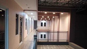A corridor with a tiled floor, a balcony with a railing, and a ceiling with exposed beams and lighting fixtures. - Karana Guesthouse Syariah Bandung & Luang Cafe (Bandung)