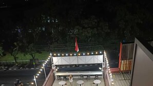 An outdoor seating area with tables and chairs, surrounded by potted plants and a flag. - Karana Guesthouse Syariah Bandung & Luang Cafe (Bandung)