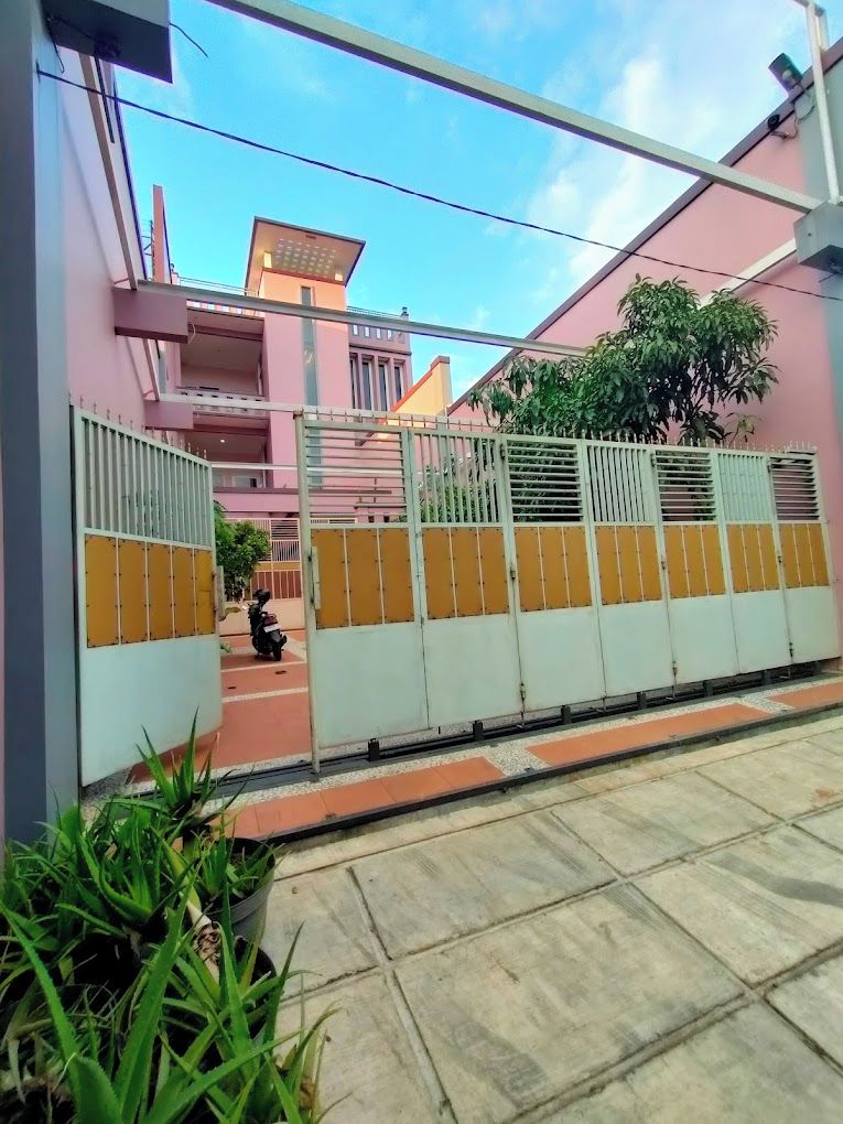 A gated entrance with a scooter parked inside, a potted plant in the foreground, and a building with a pink facade in the background.