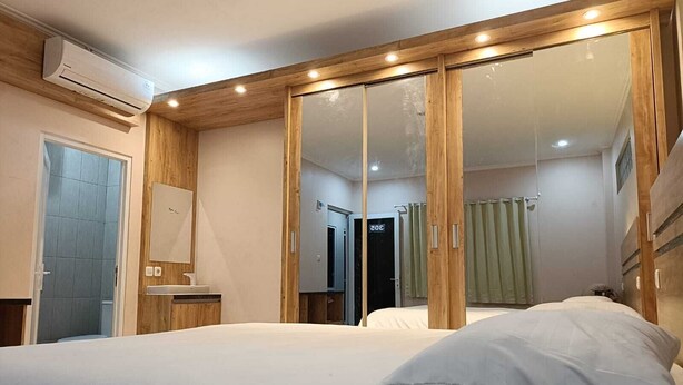 A bedroom with a bed, a mirror, a wardrobe, and an air conditioning unit. - Karana Guesthouse Syariah Bandung & Luang Cafe (Bandung)