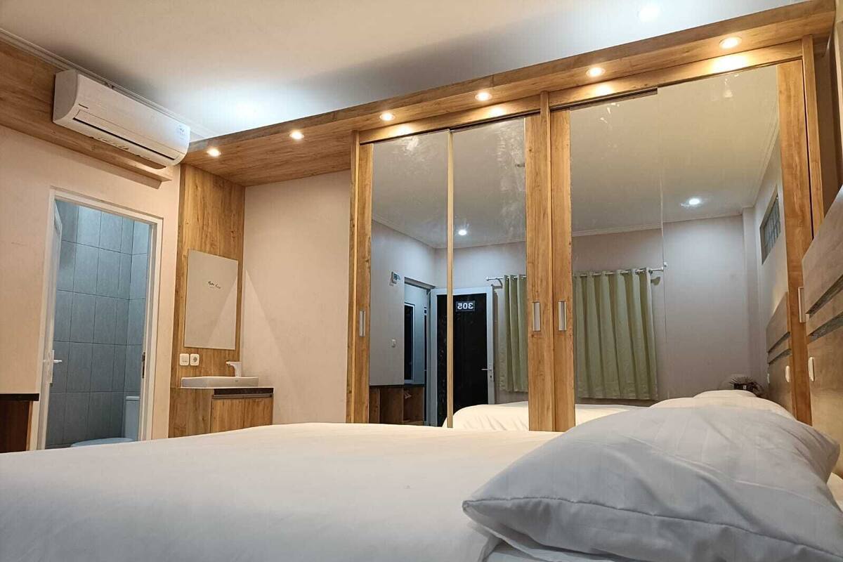 A bedroom with a bed, a mirror, a wardrobe, and an air conditioning unit.