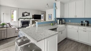 Une cuisine moderne avec des armoires blanches, un comptoir en granit et un îlot central intégré doté de tabourets de bar.