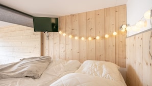 Ein Schlafzimmer mit einem Holz-Kopfteil, einem flachbildfernseher über dem Bett und Lichterketten.
