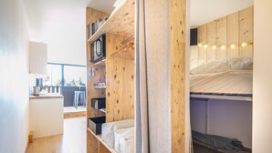 Ein kleines Zimmer mit Etagenbett, Holzregalen, Schreibtisch und Fenster.