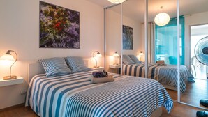 A hotel room with a large mirror, striped bedding, and a painting of flowers.