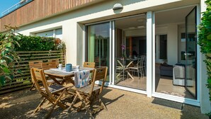 An outdoor patio with wooden furniture and a table, a sliding glass door leading to an interior space, and a wooden fence.