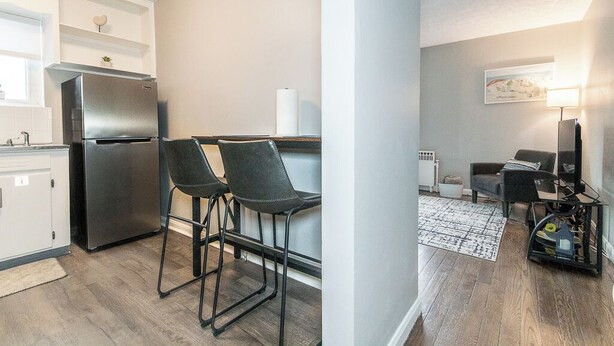 A modern kitchen with a refrigerator, two bar stools, and a dining area with a table and chairs.