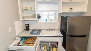 A compact kitchen with white cabinets, a stainless steel refrigerator, a window with blinds, and a built-in sink.
