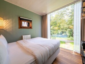 Et soveværelse med en stor seng, et vindue med gardiner, en radiator og en vægmonteret hylde med en lampe.