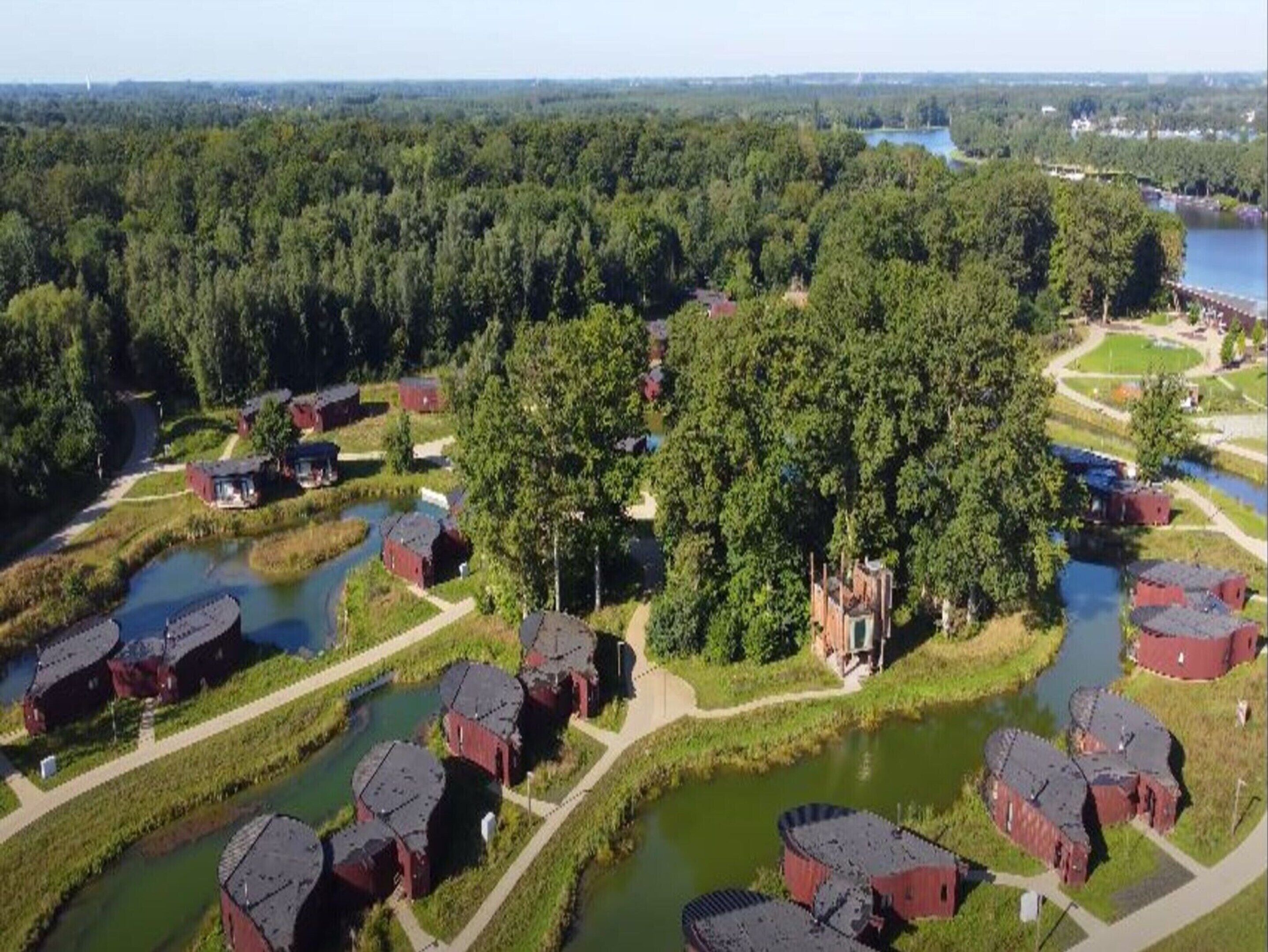 A rural area with several red-roofed buildings, likely barns or farmhouses, surrounded by dense forest and a river.