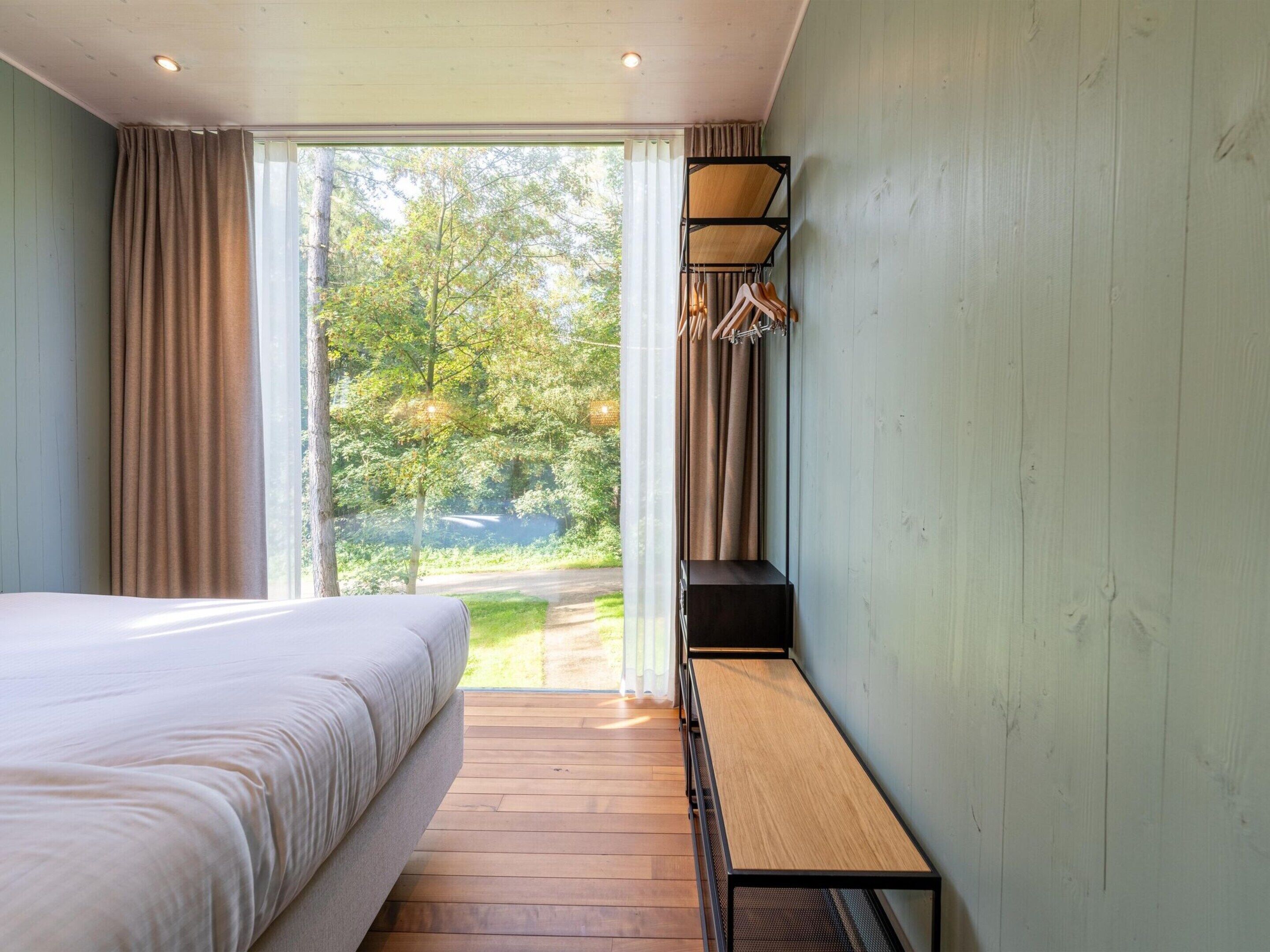 Ein Schlafzimmer mit Bett, Sitzbank und Blick auf Grün.