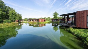 Un domaine paisible au bord d’un lac, avec des chalets en bois, une étendue d’eau aux reflets changeants et une végétation luxuriante.