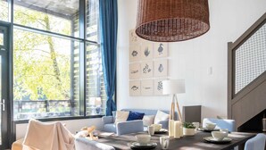 A dining area with a wooden table, light blue chairs, and a hanging wicker lamp. - Getaway With Pool Access (Antoing)