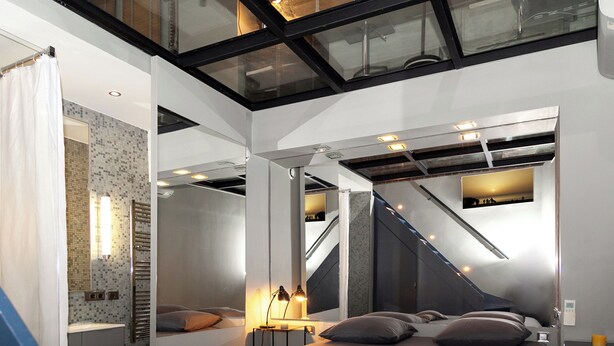 Une chambre moderne avec un grand lit, un miroir, une petite table avec des lampes et un escalier menant à un niveau supérieur.