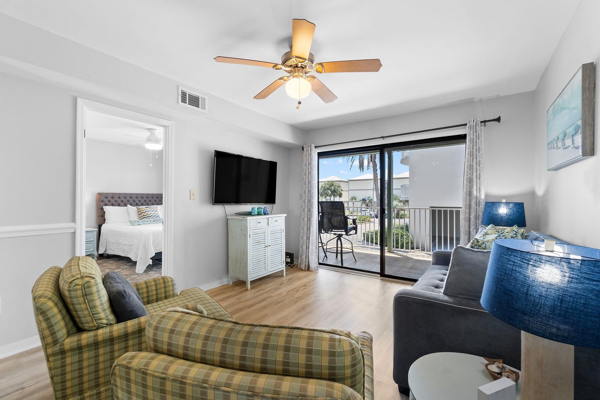 A living room with a ceiling fan, a sofa, a TV, and a view of the outside.