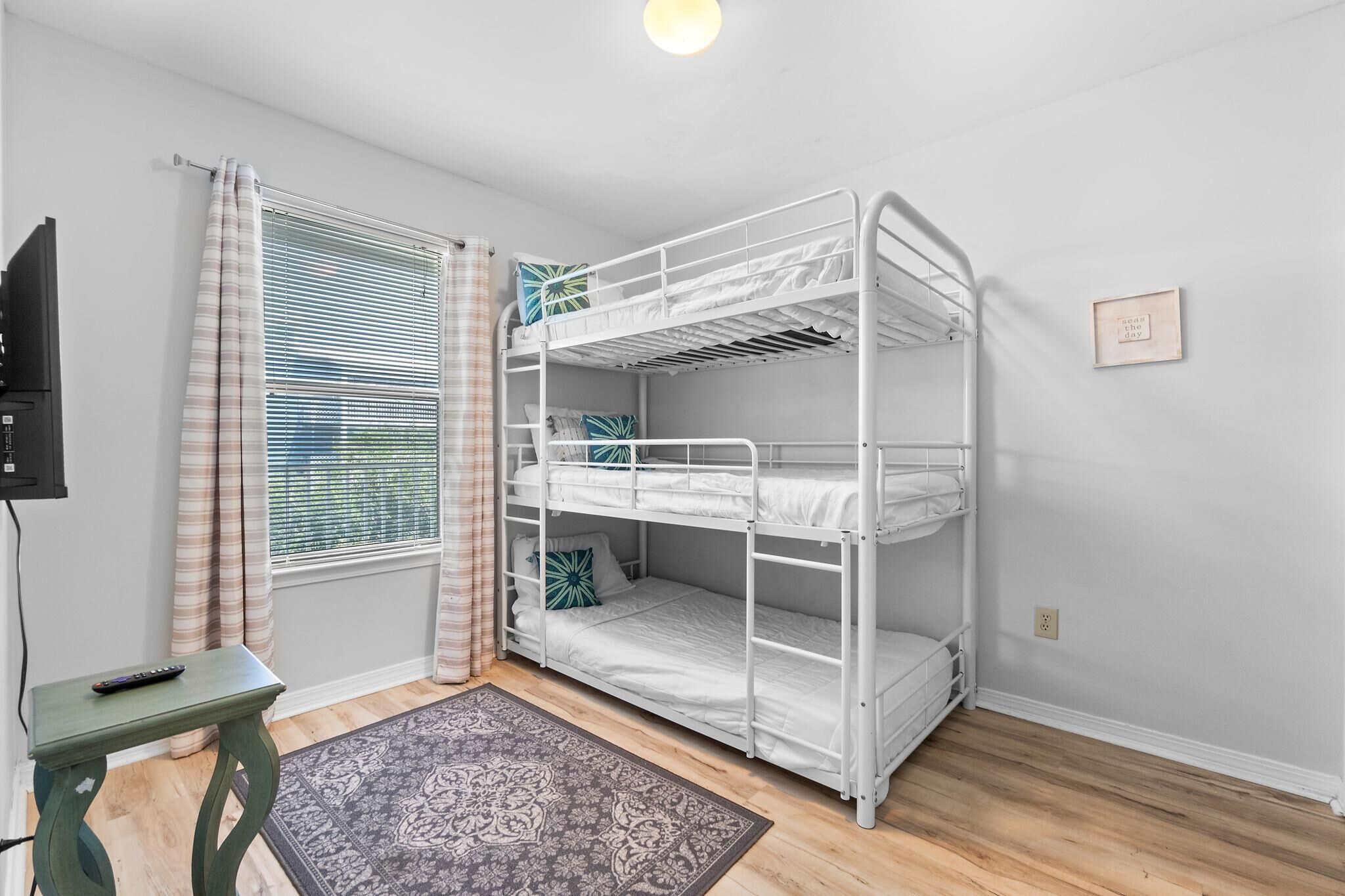 A bunk bed room with a TV, a small table, and a window with blinds.