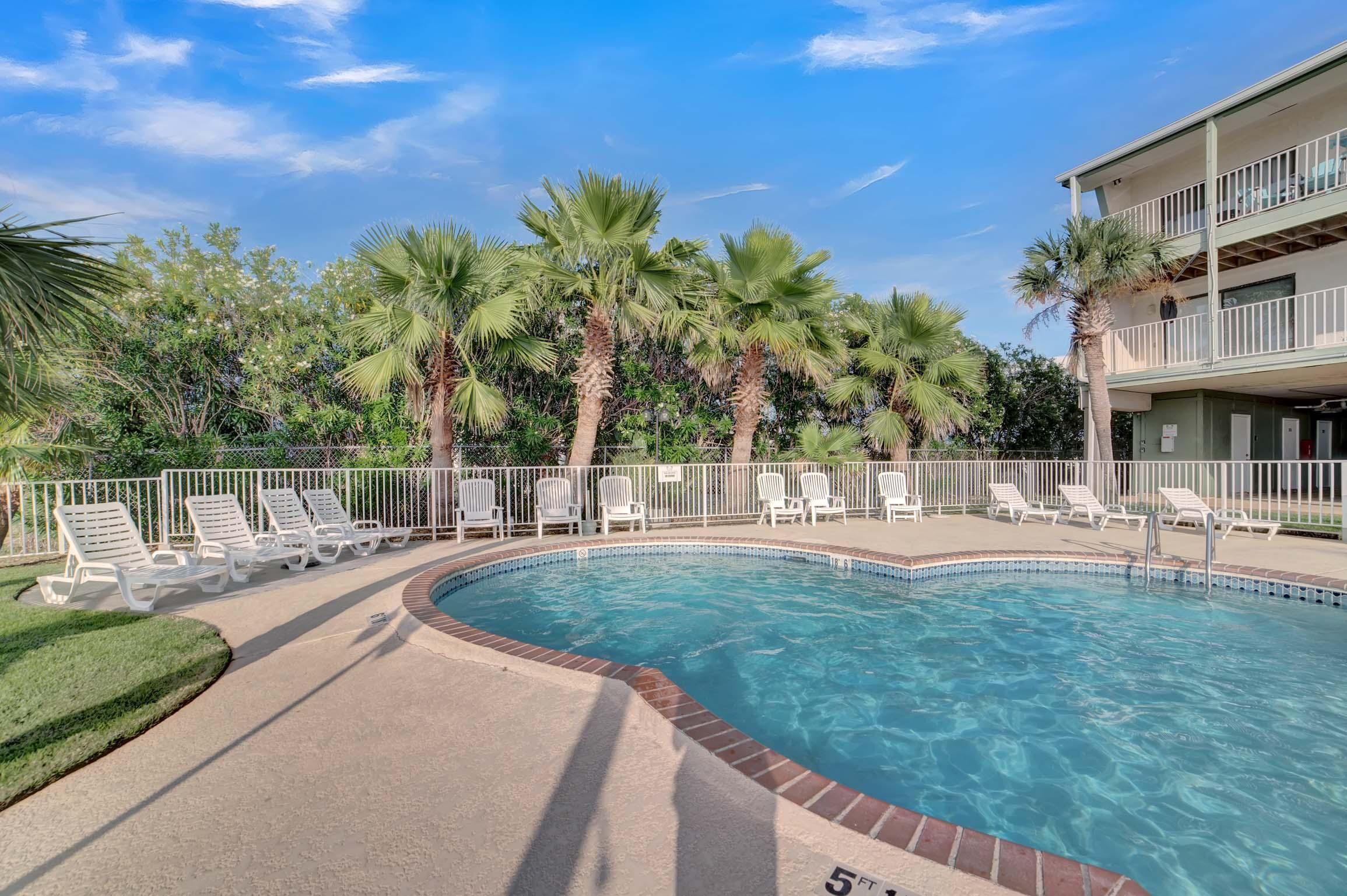 A swimming pool with lounge chairs, palm trees, and a building with a balcony.