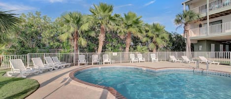 A swimming pool with lounge chairs, palm trees, and a building with a balcony.