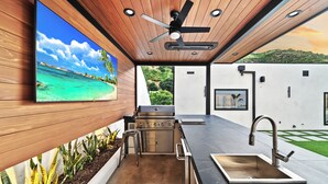 Une cuisine extérieure équipée d’un barbecue, d’un évier et d’un ventilateur de plafond.