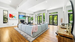 Un salon moderne doté d’un grand canapé d’angle, d’une cheminée et de grandes fenêtres offrant une vue sur la verdure.