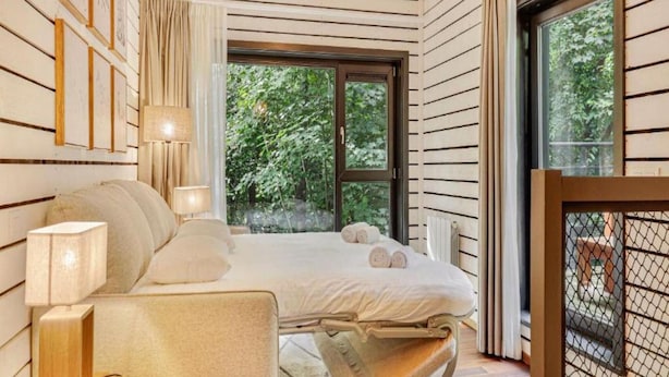 Une chambre à coucher avec un lit, des lampes de chevet, une chaise et une fenêtre donnant sur des arbres.