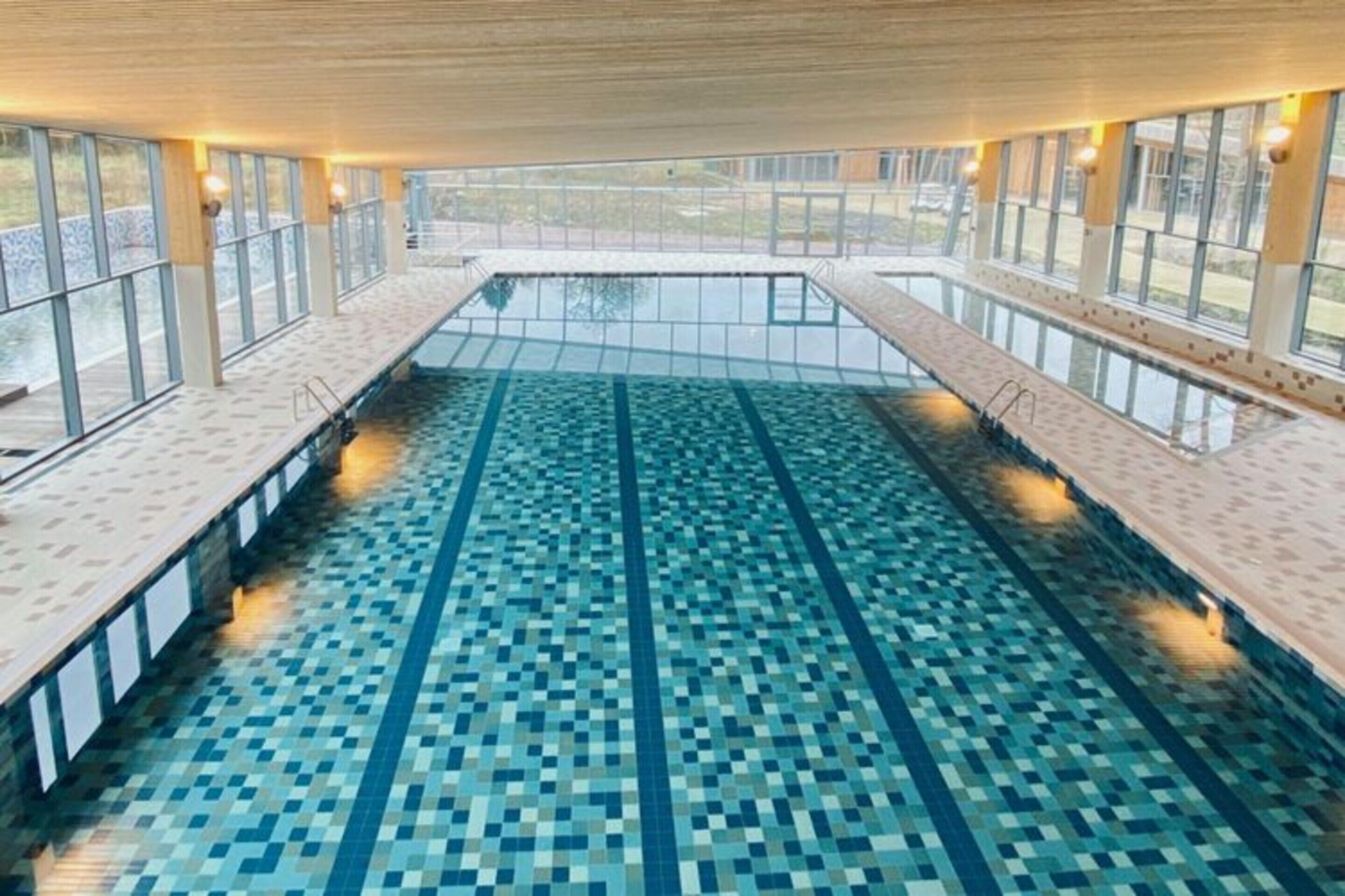 En inomhuspool med ett kaklat golv och utsikt över omgivningen genom stora fönster.