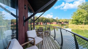 Une terrasse en bois avec des sièges extérieurs, offrant une vue sur une étendue d’eau calme et une zone boisée.