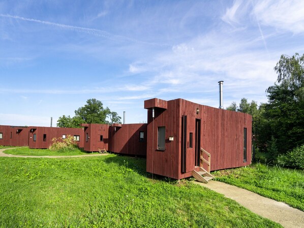 Une rangée de cabanes en bois rouges, avec un ciel dégagé et une végétation luxuriante en arrière-plan.
