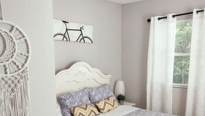 Un dormitorio ordenado con una cama, un adorno de macramé en la pared y una obra de arte con motivos de bicicleta.