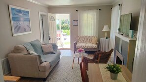 Una sala de estar con un sofá, una mesa de comedor con sillas, una televisión y una puerta que da al exterior.
