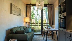 A cozy room with a green sofa, a wooden dining table, and a kitchen area with cabinets and a stove. - Idyllic Nature Lodge by Belvilla (Antoing)