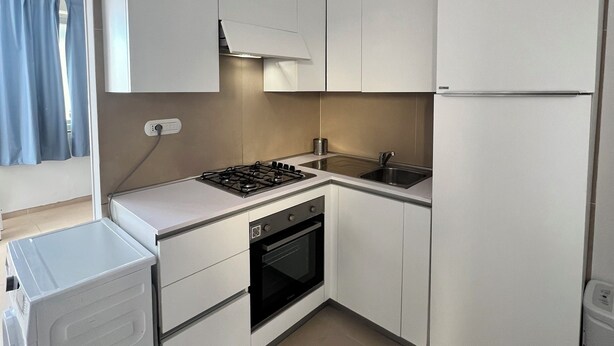 A compact kitchen with white cabinets, a gas stove, an oven, a sink, and a built-in refrigerator. - Casa Castagna a' Mare (Salerno)