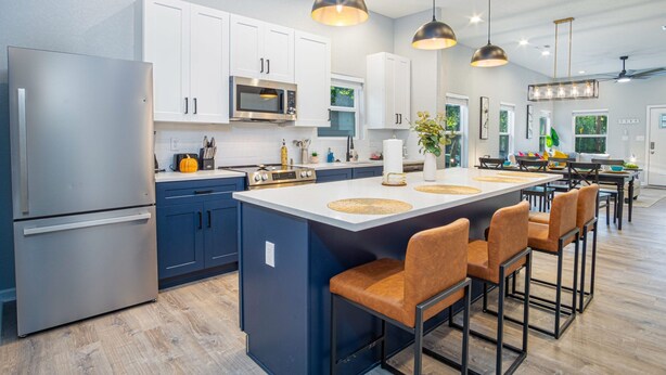 Eine moderne Küche mit weißen Schränken, Edelstahlgeräten und einer zentralen Kochinsel mit Barhocker.