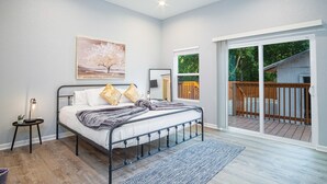 Ein Schlafzimmer mit Bett, Deckenventilator, Nachttisch, Gemälde und Blick auf eine Terrasse durch eine Glastür.