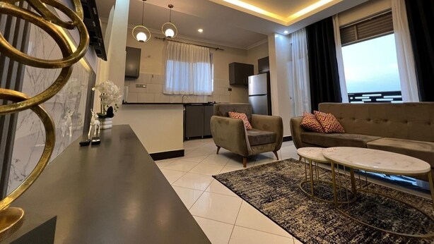 Ein modernes Wohnzimmer mit einer Couch, Sesseln, einem Couchtisch und einer Küche im Hintergrund.