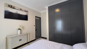 Ein Schlafzimmer mit einem großen Bett, einem Kleiderschrank, einem Konsolentisch mit einer Vase und einem Bild an der Wand.