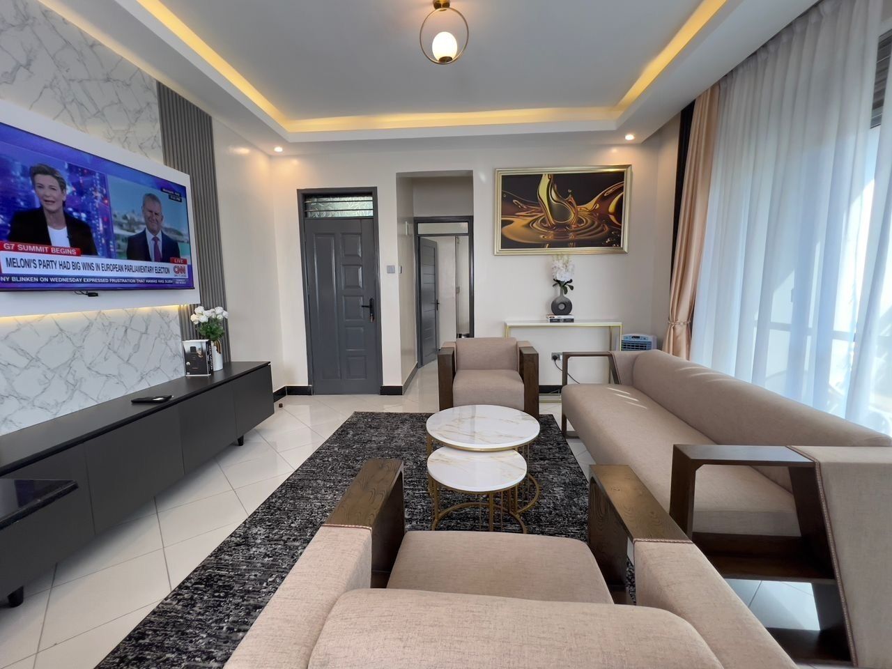A modern living room with a flat-screen TV, a sofa, two round coffee tables, and a marble-patterned rug.