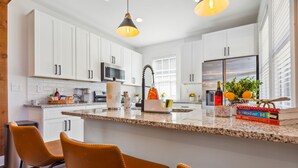 A modern kitchen with white cabinets, a granite countertop, and a central island with chairs. - NEW ATL Bungalow-Sun Room-BBQ-King Bed-Fenced Yard (Atlanta)