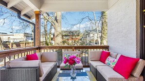 A covered outdoor seating area with wicker furniture and a glass table, featuring a vase of flowers. - NEW ATL Bungalow-Sun Room-BBQ-King Bed-Fenced Yard (Atlanta)