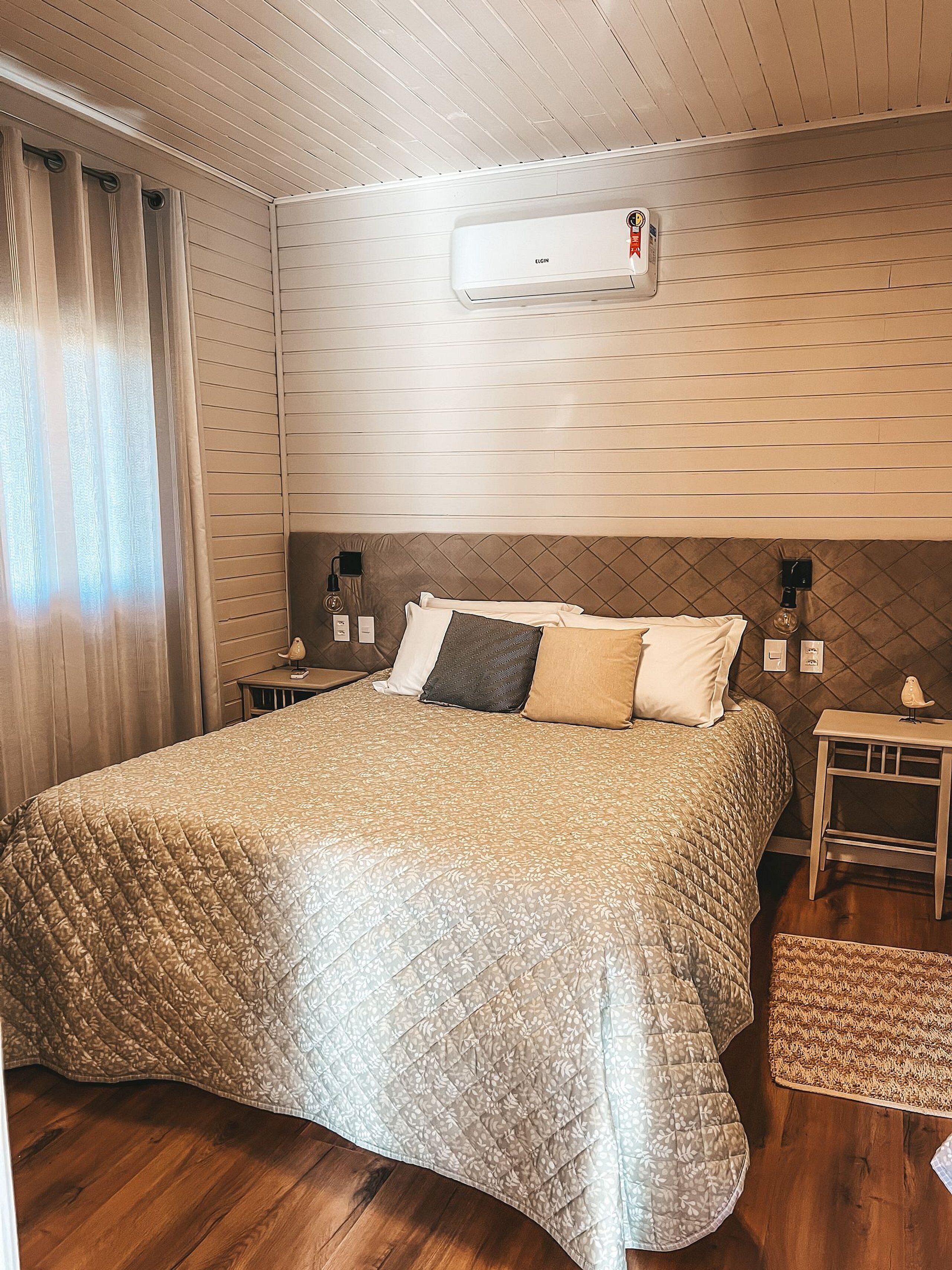 Un dormitorio ordenado con una cama grande, aire acondicionado instalado en la pared y una mesita de noche con lámpara.